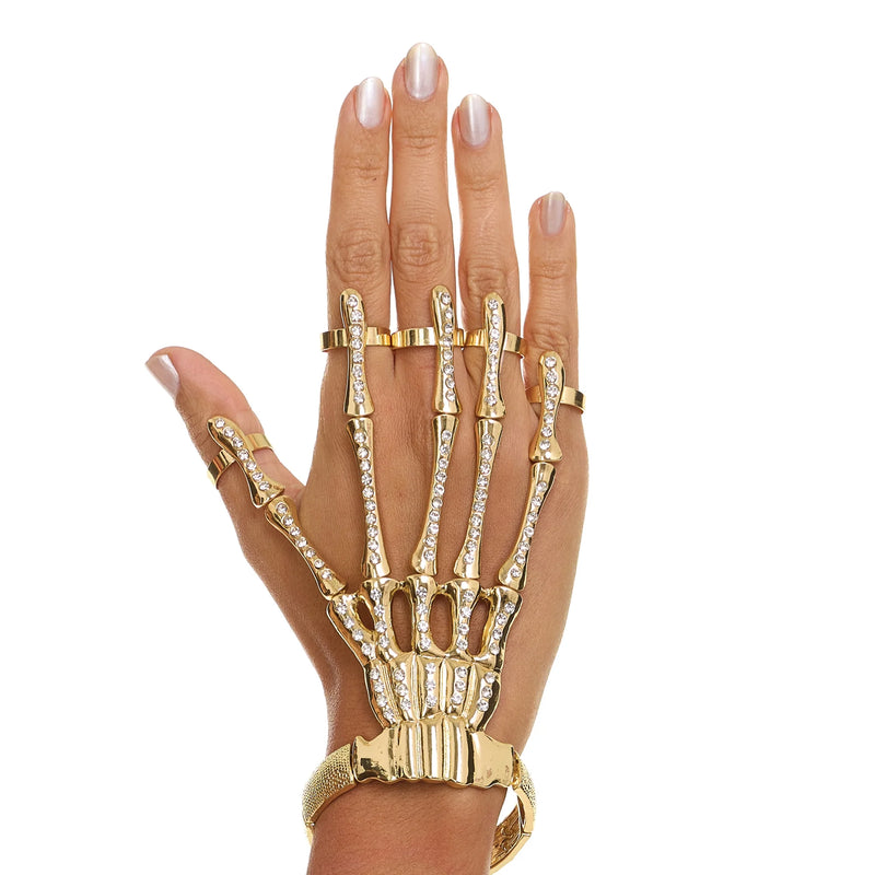 Hand wearing a gold skeleton ring with clear stones on a white background