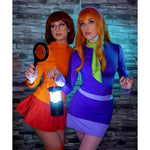Two people in colorful costumes holding props against a stone wall background